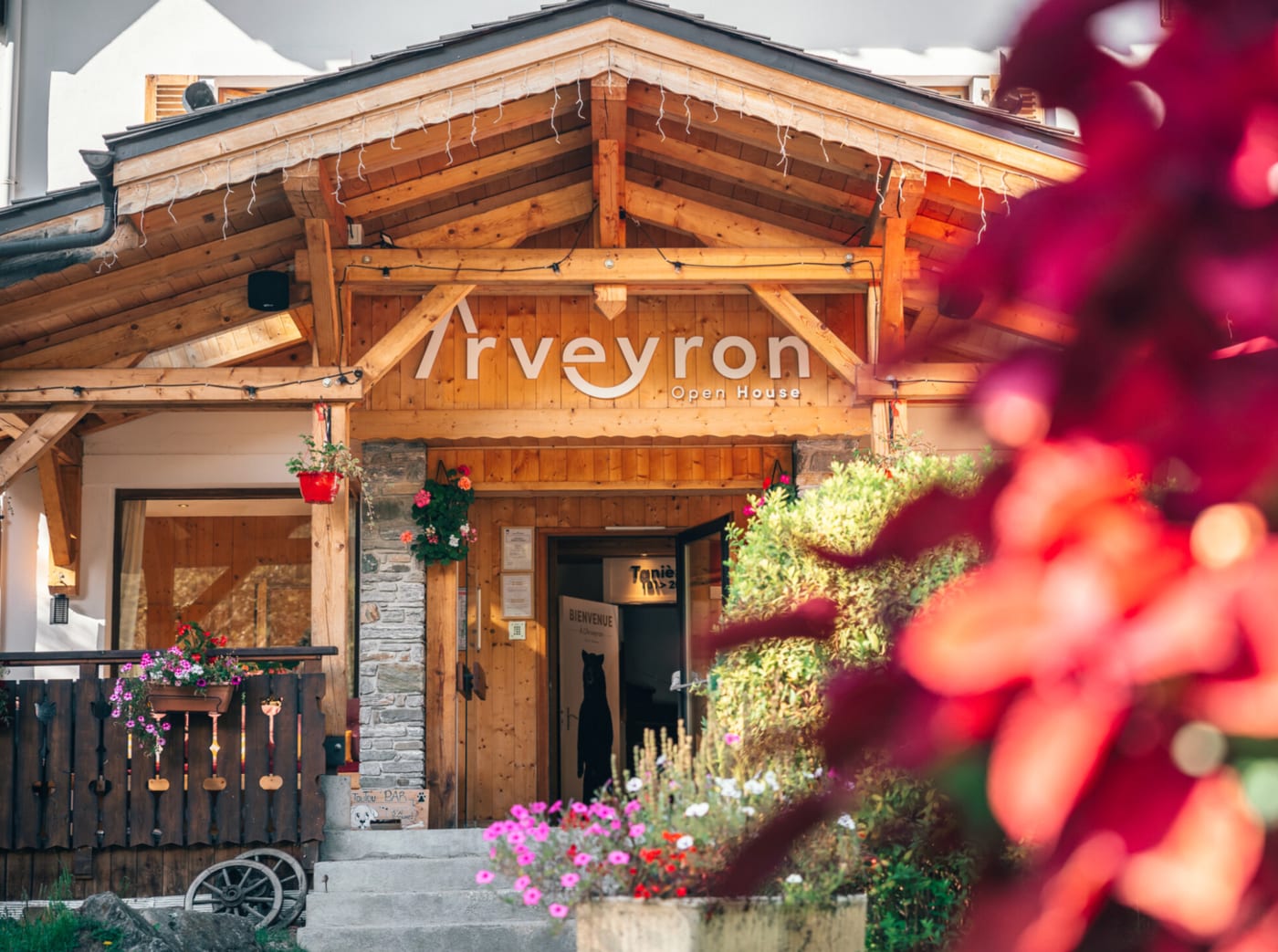 L'Arveyron Open House à Chamonix, façade en bois alpin entourée de fleurs, au cœur d'une forêt de sapins